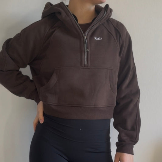 Person wearing a brown pullover with a brand logo against a plain background